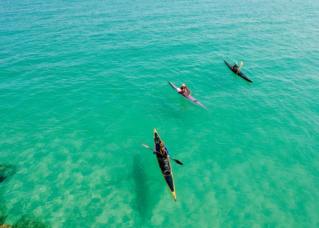 Three kayakers paddle through pristine, turquoise ocean waters, enjoying a sunny outdoor adventure.